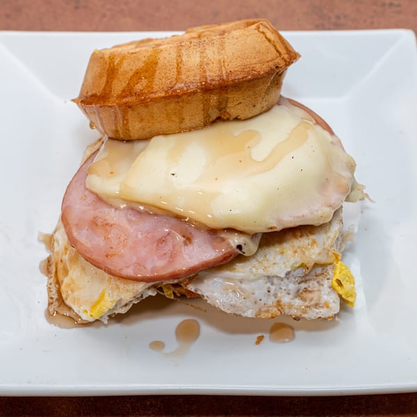 Ida's Cafe breakfast sandwich with waffle, ham, fried egg, cheese, and syrup on a white plate.