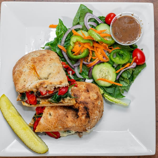 Ida's Cafe breakfast panini with roasted vegetables, melted cheese, a side salad, and a pickle.