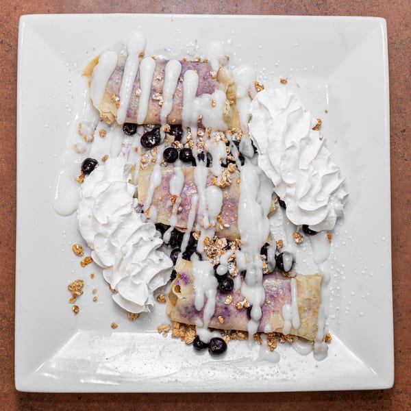 Three blueberry crepes topped with white icing, whipped cream, granola, and fresh blueberries.