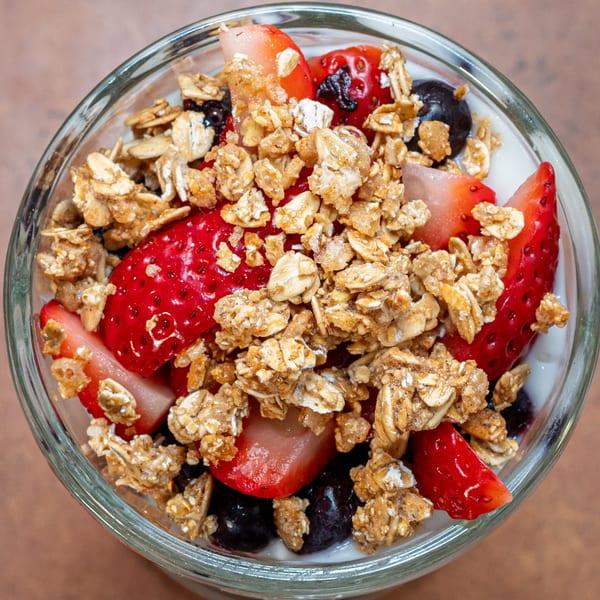 Overhead view of a glass bowl filled with yogurt, strawberries, blueberries, and granola.